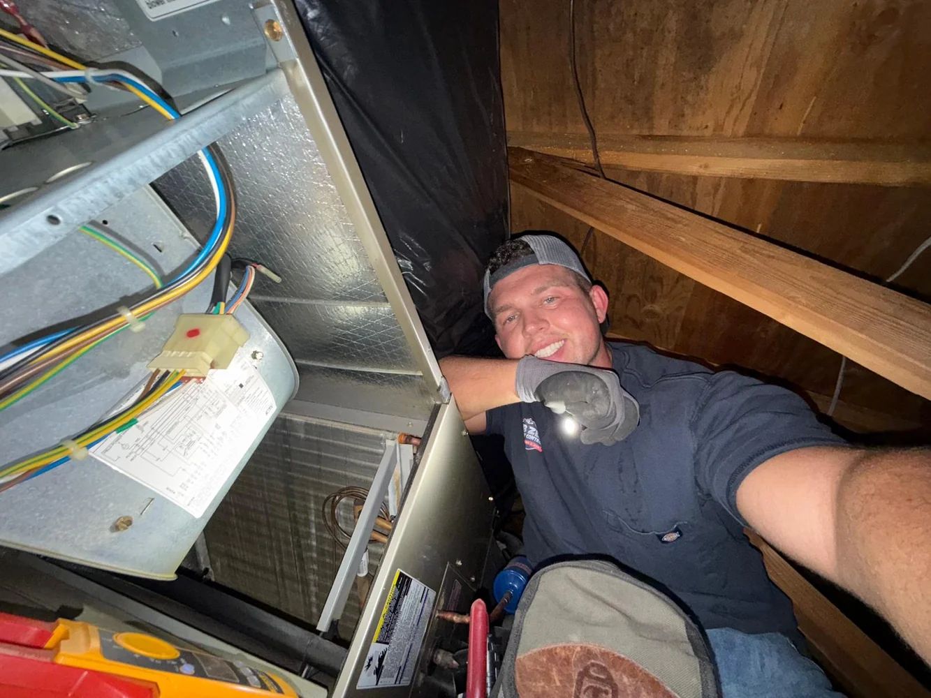 Technician checking wiring and evaporator coil in an attic